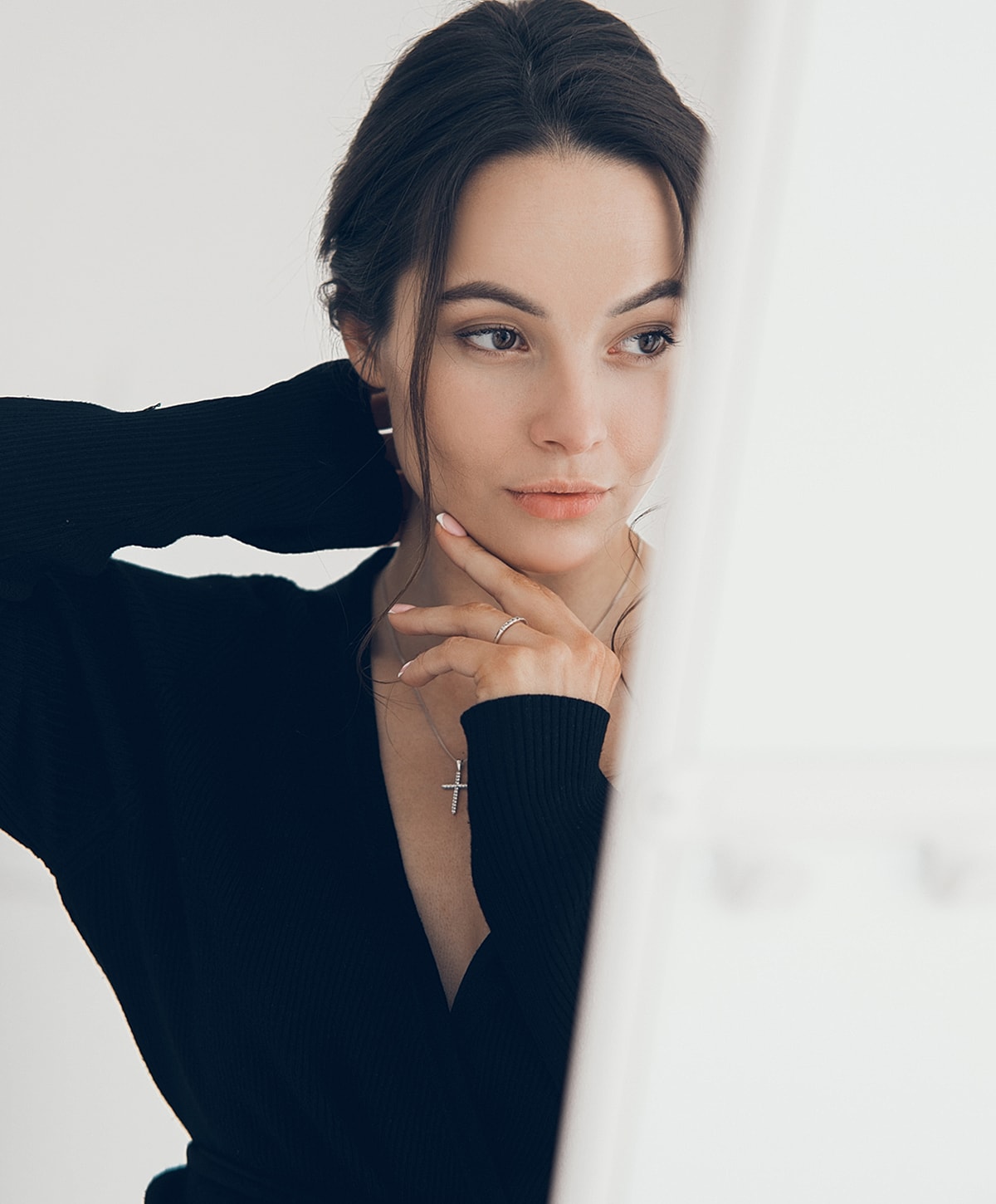 Woman in black sweater touching her face thoughtfully.